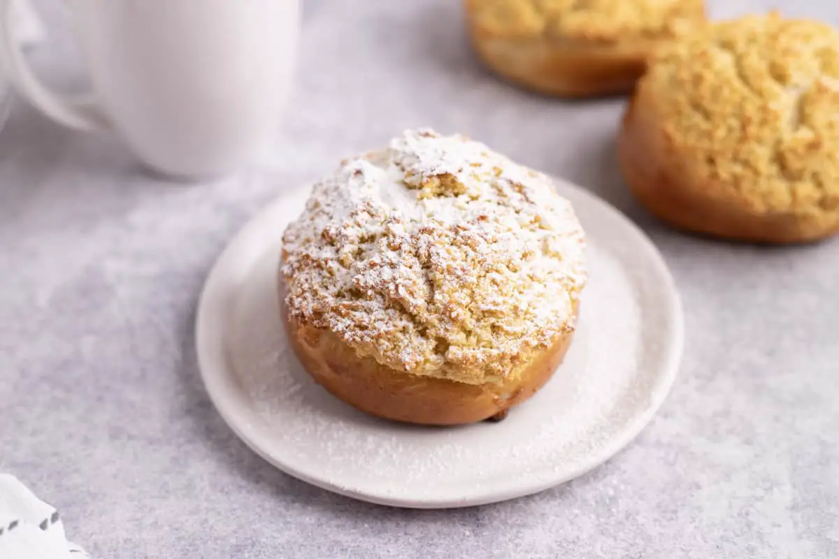 Pão De Deus served on a white plate with icing sugar sprinkled on top.