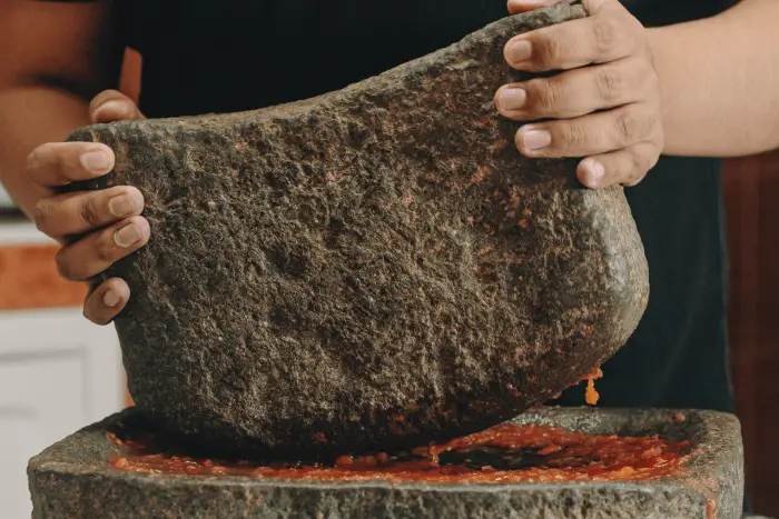 una persona moliendo verduras entre dos piedras