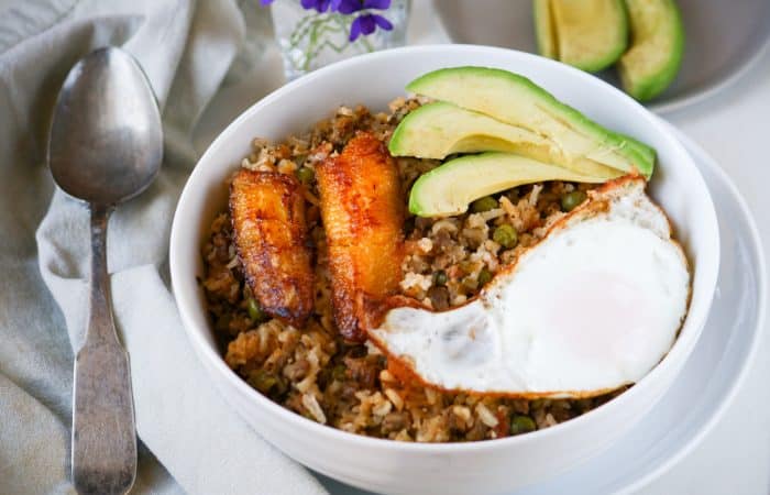 fried rice in a bowl with plantain, fried egg, and avocado