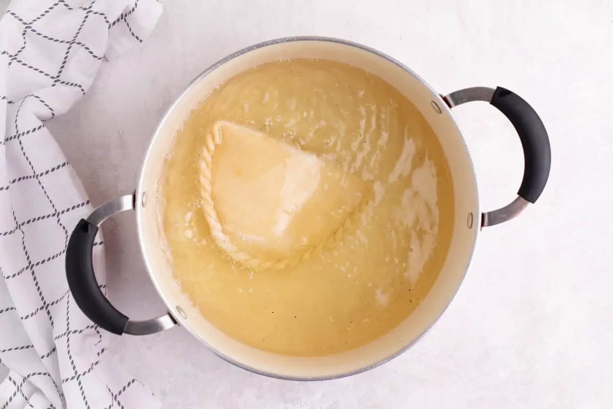 olla con aceite fritando empanada boliviana de queso