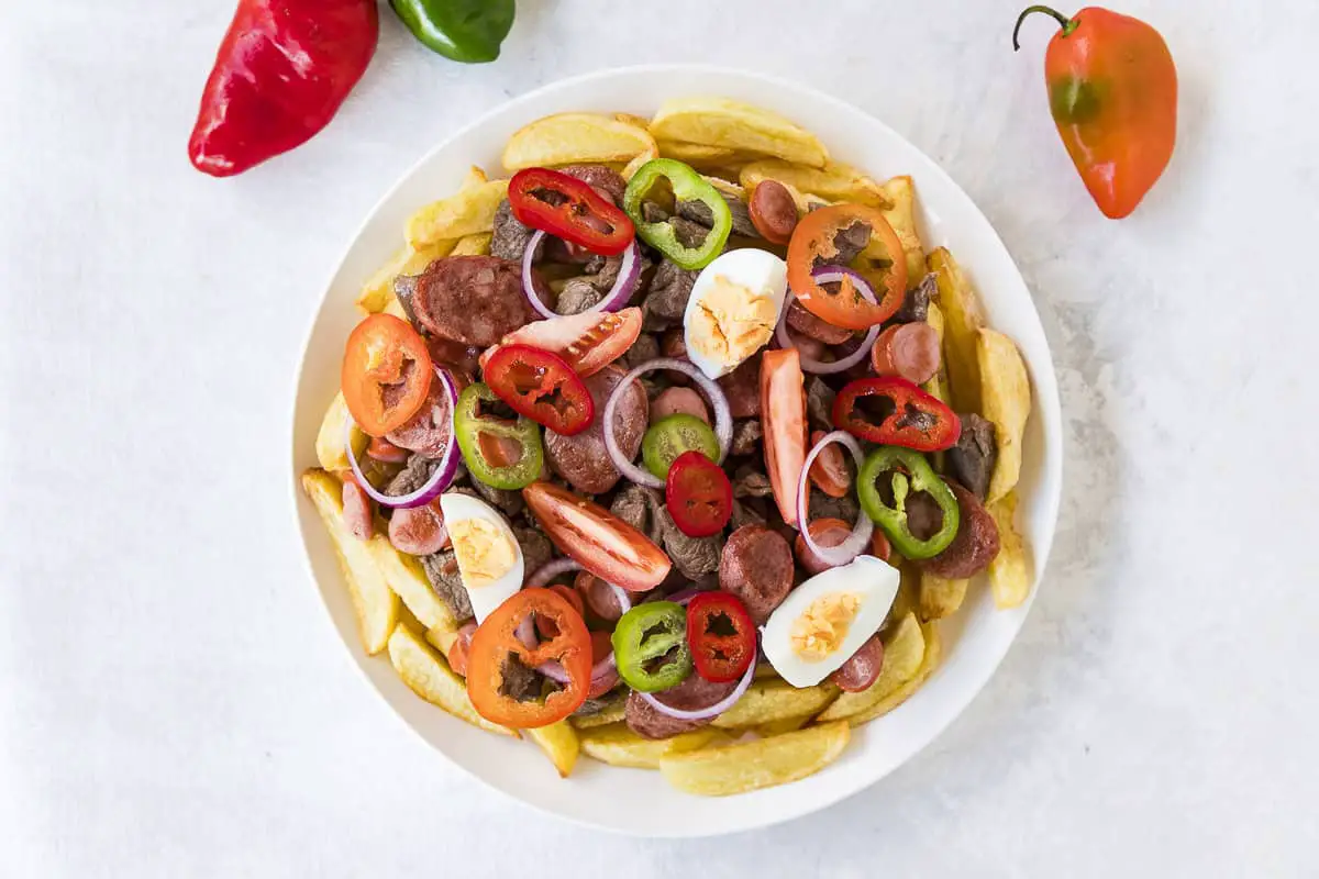plato de pique a lo macho boliviano con papas fritas, carne, chorizos, salchichas, cebolla, tomate, huevo duro, y aji